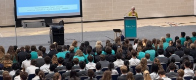 A woman stands behind a lectern speaking to a large audience of Stephen Perse Cambridge students about European Day or Languages 2026. 